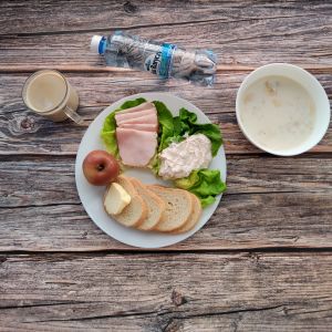 Zdjęcie przedstawia Dietę łatwostrawną:  Kawa zbożowa z mlekiem Owsianka budyniowa z bananem i jabłkiem z posypką chia Bułka pszenna długa krojona Masło extra Szynka Piastowska Sałata zielona Woda mineralna Jabłko pieczone Twarożek różany 